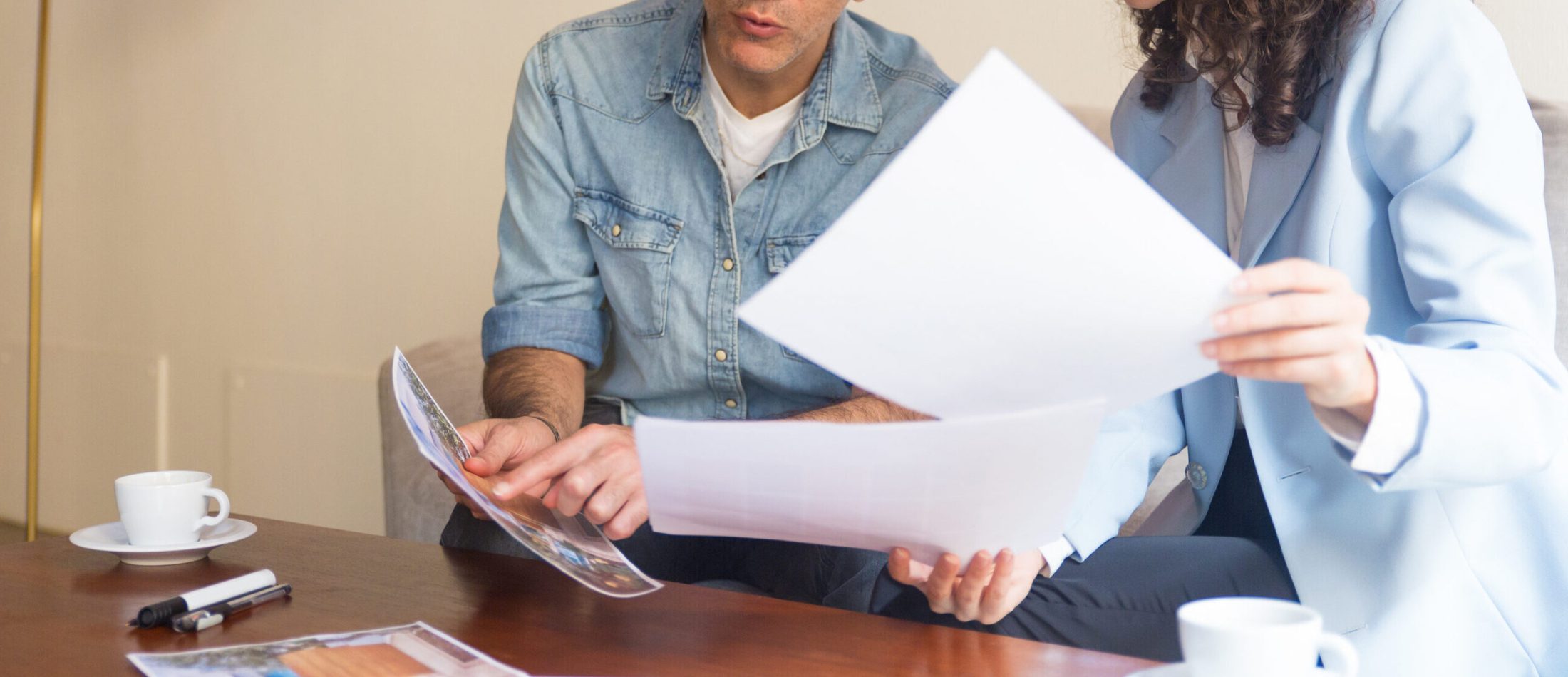 Design professional and home owner studying sketches, drafts and drawings for renovation project. Man and woman sitting in living room at home and talking. Interior designer work concept