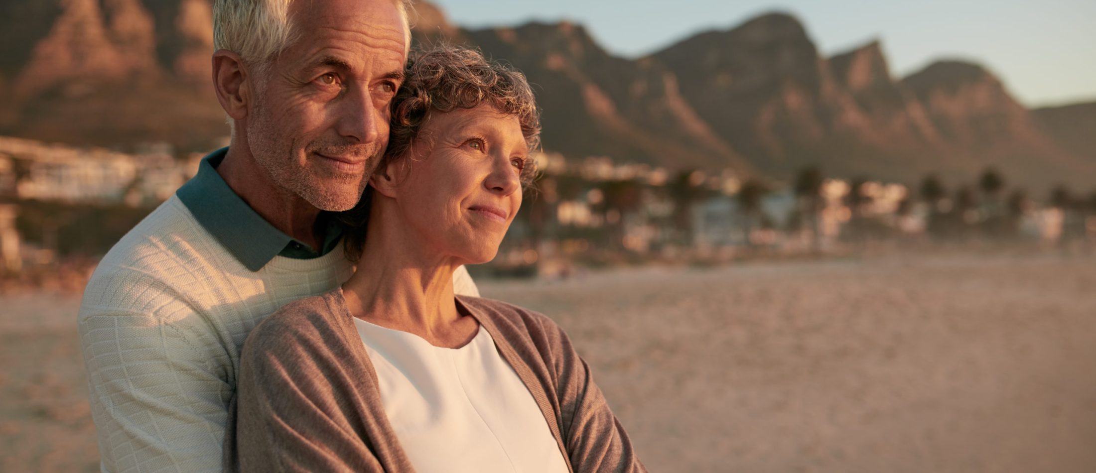 Portrait of elderly couple standing together and embracing on the beach. Senior man embracing his beautiful wife and looking away at a view.