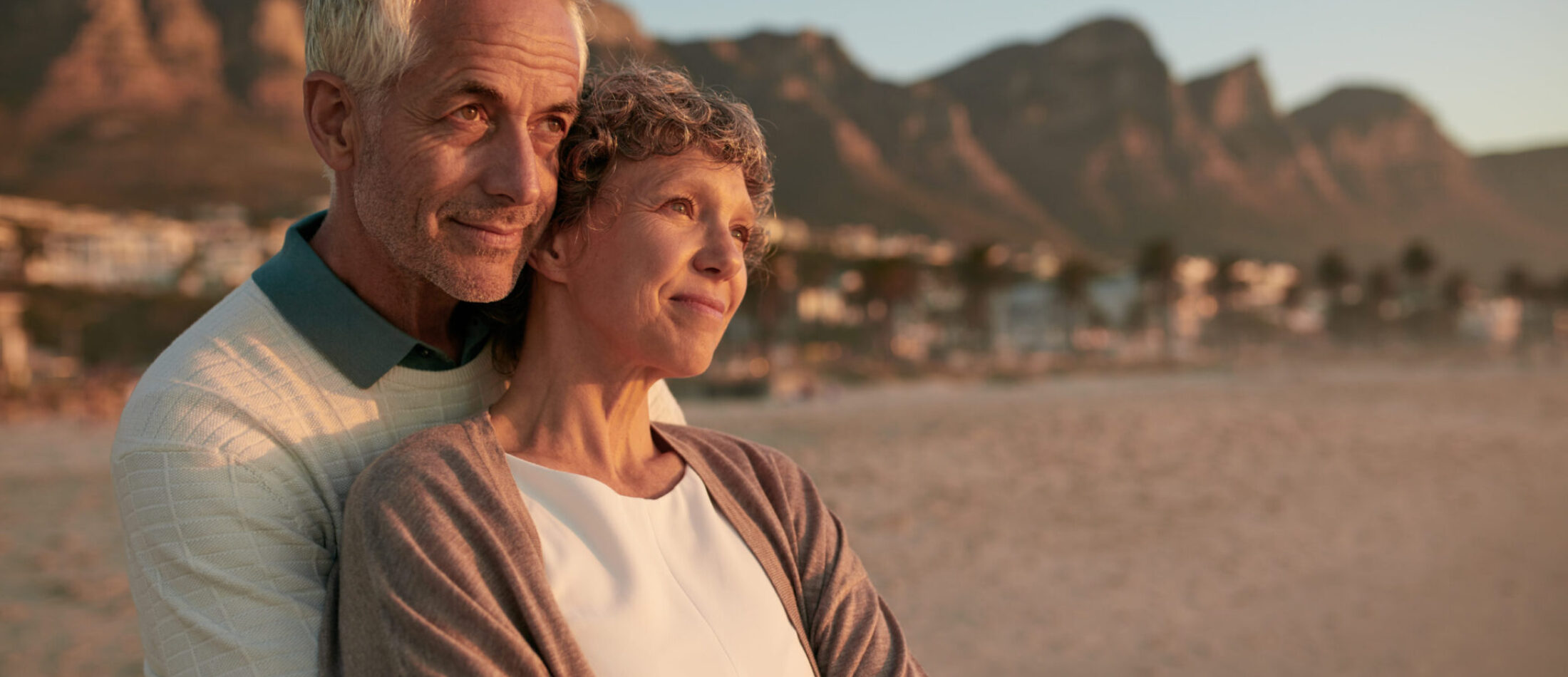 Portrait of elderly couple standing together and embracing on the beach. Senior man embracing his beautiful wife and looking away at a view.
